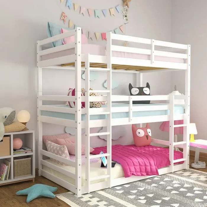 A white bunk bed occupies a cozy children's room, featuring pastel bedding and decorative pillows. Colorful banners and stuffed animals enhance the playful atmosphere.