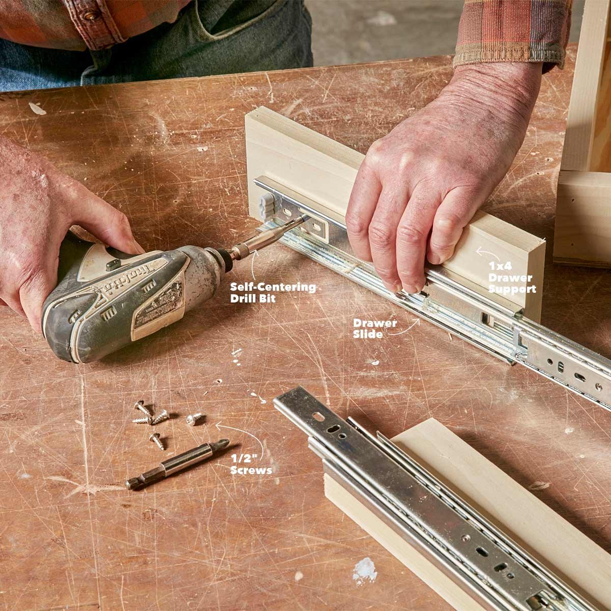 A person uses a drill to attach a metal drawer slide to a wooden support on a workbench, surrounded by tools and screws.