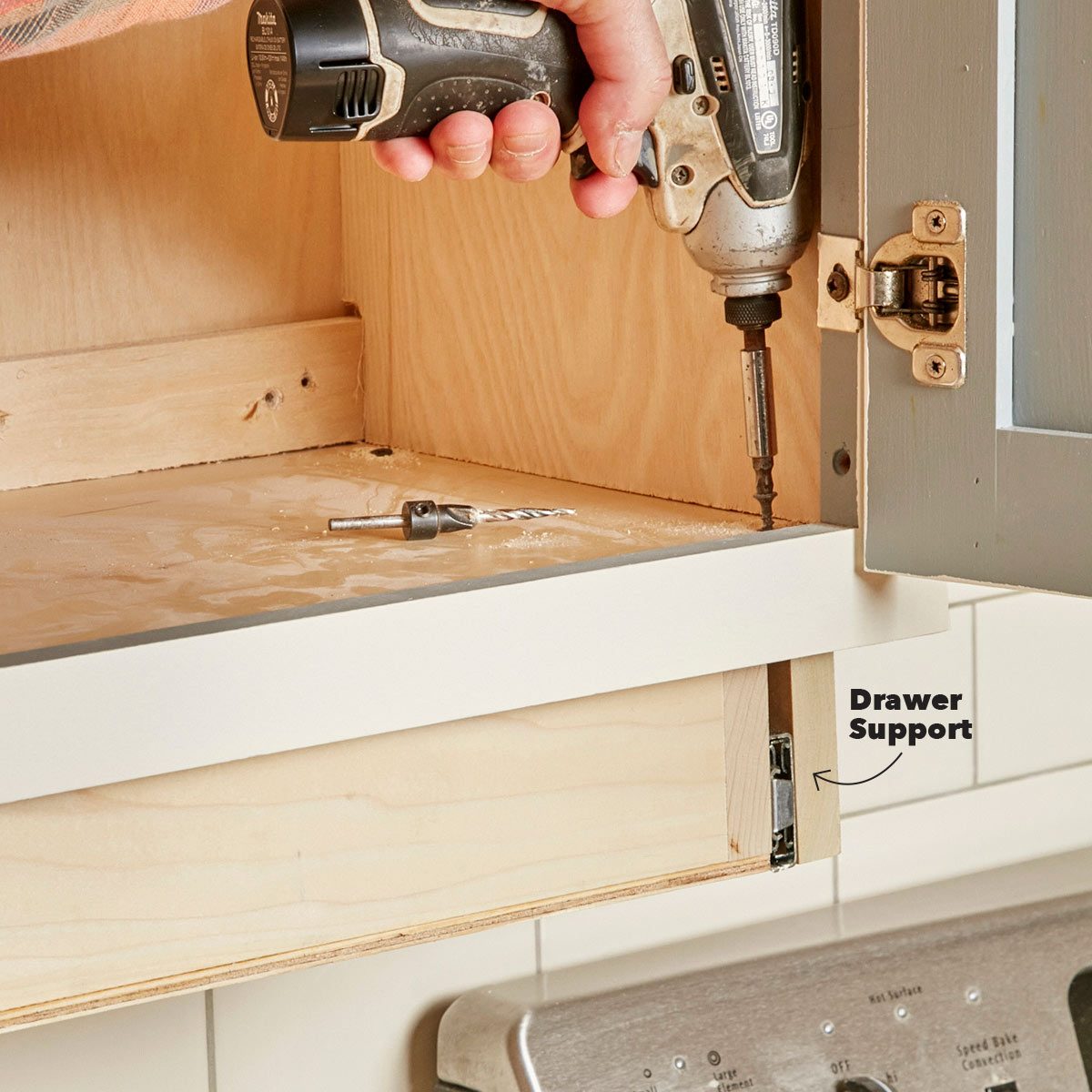 A hand holds a power drill, fastening a screw into a cabinet inside. A metal drawer support is visible, alongside a countertop.