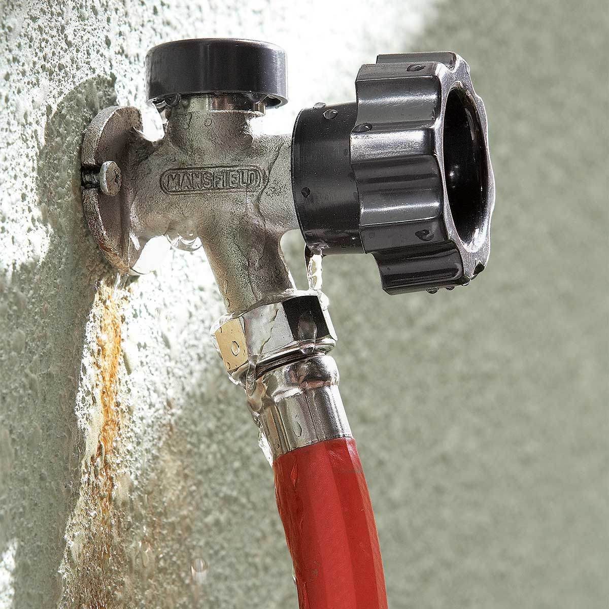 A metallic water faucet is leaking and attached to a red hose, mounted on a textured green wall. Water drips from the faucet and hose connection.
