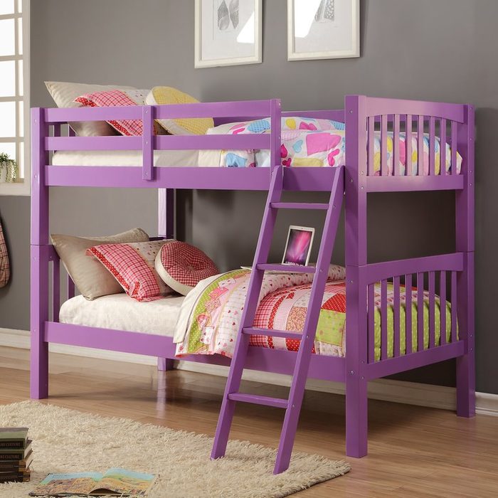 A purple bunk bed stands in a cozy room, featuring colorful bedding on both levels and a small ladder for access. Books rest on the floor nearby.