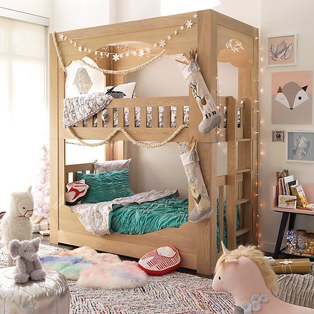A wooden bunk bed is decorated with garlands and stockings, while colorful plush toys are scattered on a patterned rug in a cozy room setting.