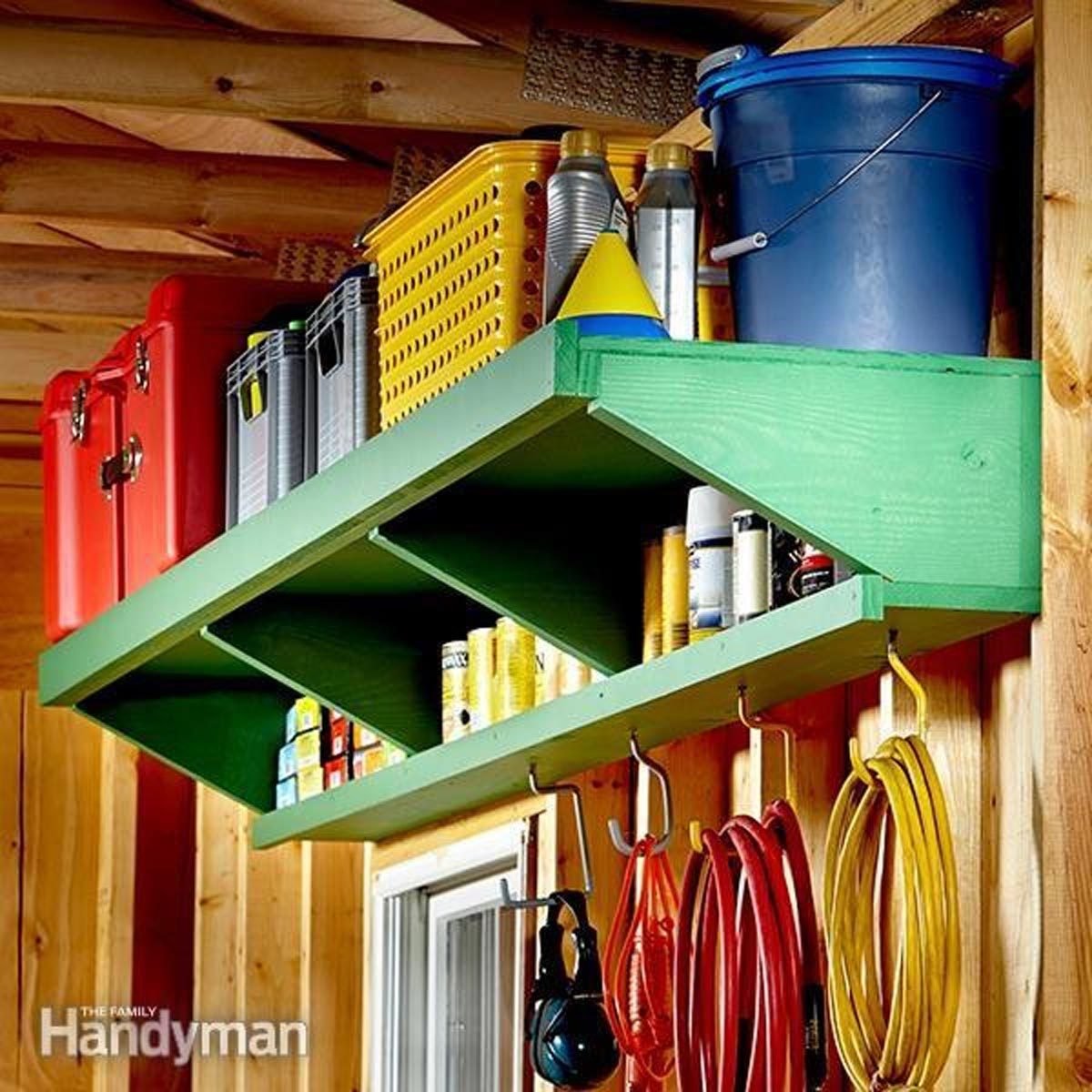 A green shelf holds various storage containers, tools, and paint cans, organized above hooks displaying hoses, all set in a wooden garage environment.