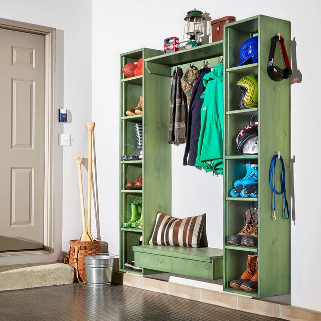 A green storage unit holds clothes, shoes, and equipment, with a bench below. It’s placed near a door, with paddles and a bucket nearby.