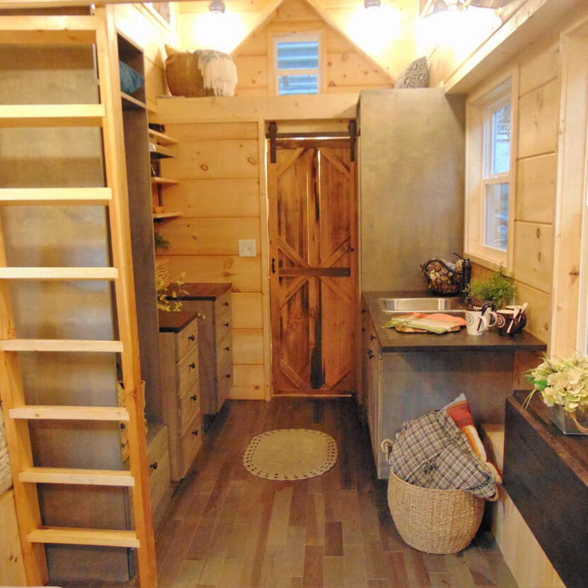 A wooden ladder leans against a wall, while a rustic kitchen features shelves, a sink, and a sliding wooden door, all in a cozy cabin atmosphere.