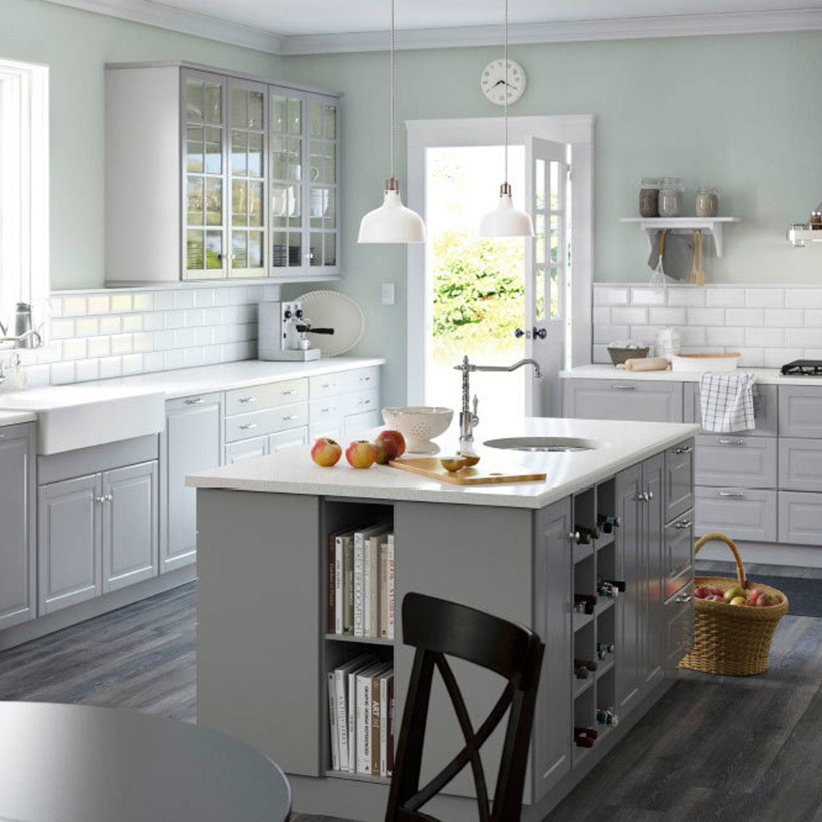 A modern kitchen features a central island with apples, sleek cabinetry, and large windows, allowing natural light to illuminate the space.