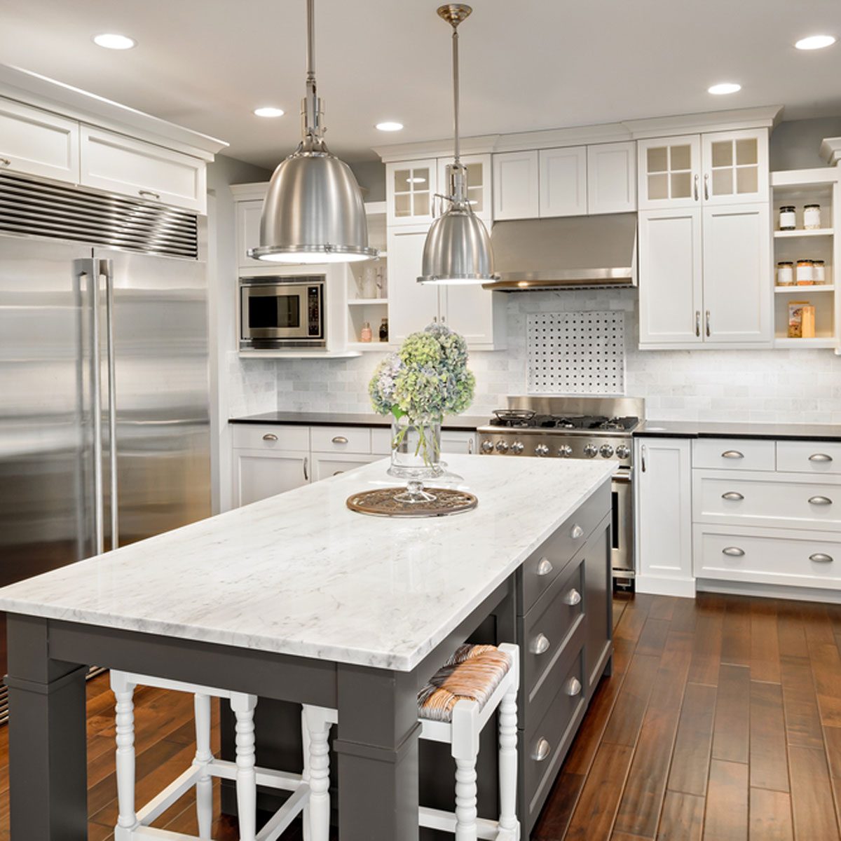 A kitchen features a marble island with a floral centerpiece, while stainless steel appliances and white cabinetry create an elegant, modern atmosphere with warm wooden floors.