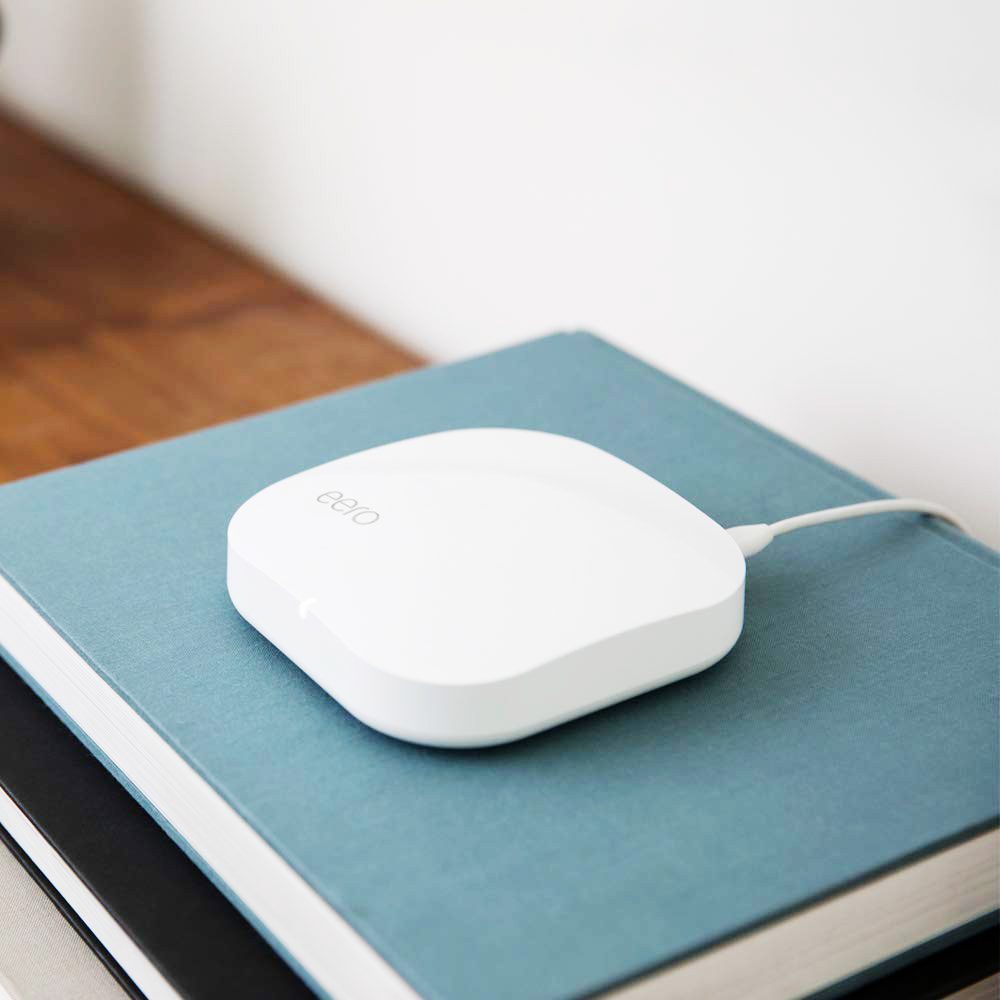 A white wireless device rests on a teal-covered notebook, connected by a cable, atop a stack of books on a wooden surface.