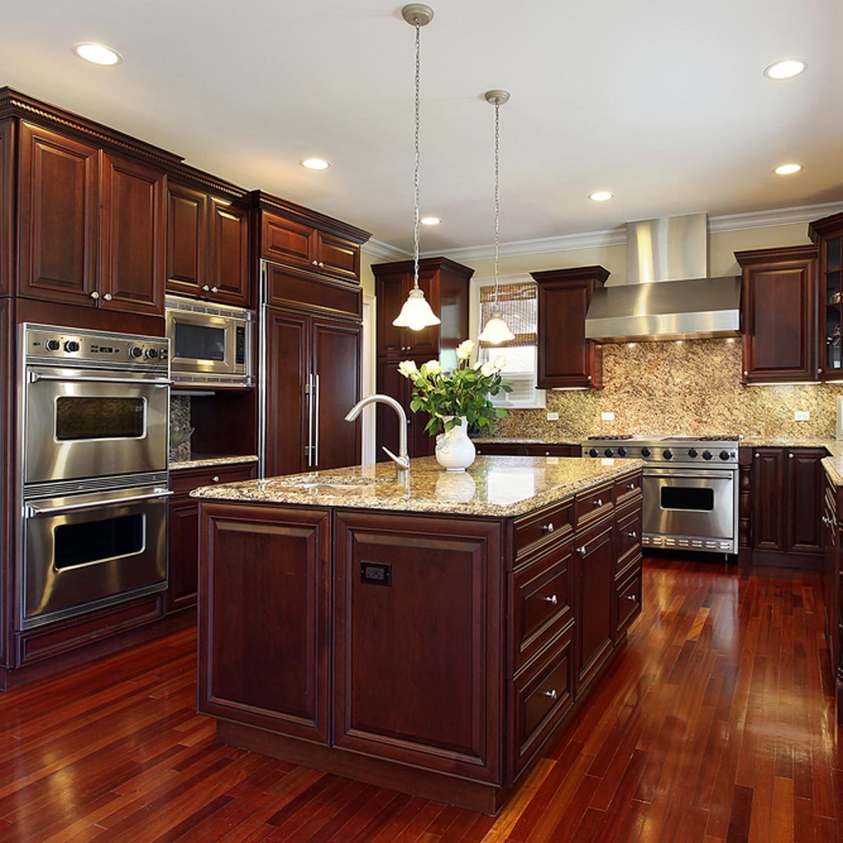 A modern kitchen features dark wood cabinetry and a central island with a granite countertop, surrounded by stainless steel appliances and warm pendant lighting.