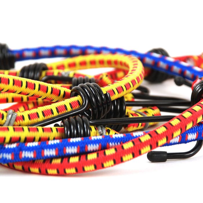 Colorful bungee cords are intertwined, featuring black hooks and coiled sections, lying on a light surface, suggesting readiness for securing items.
