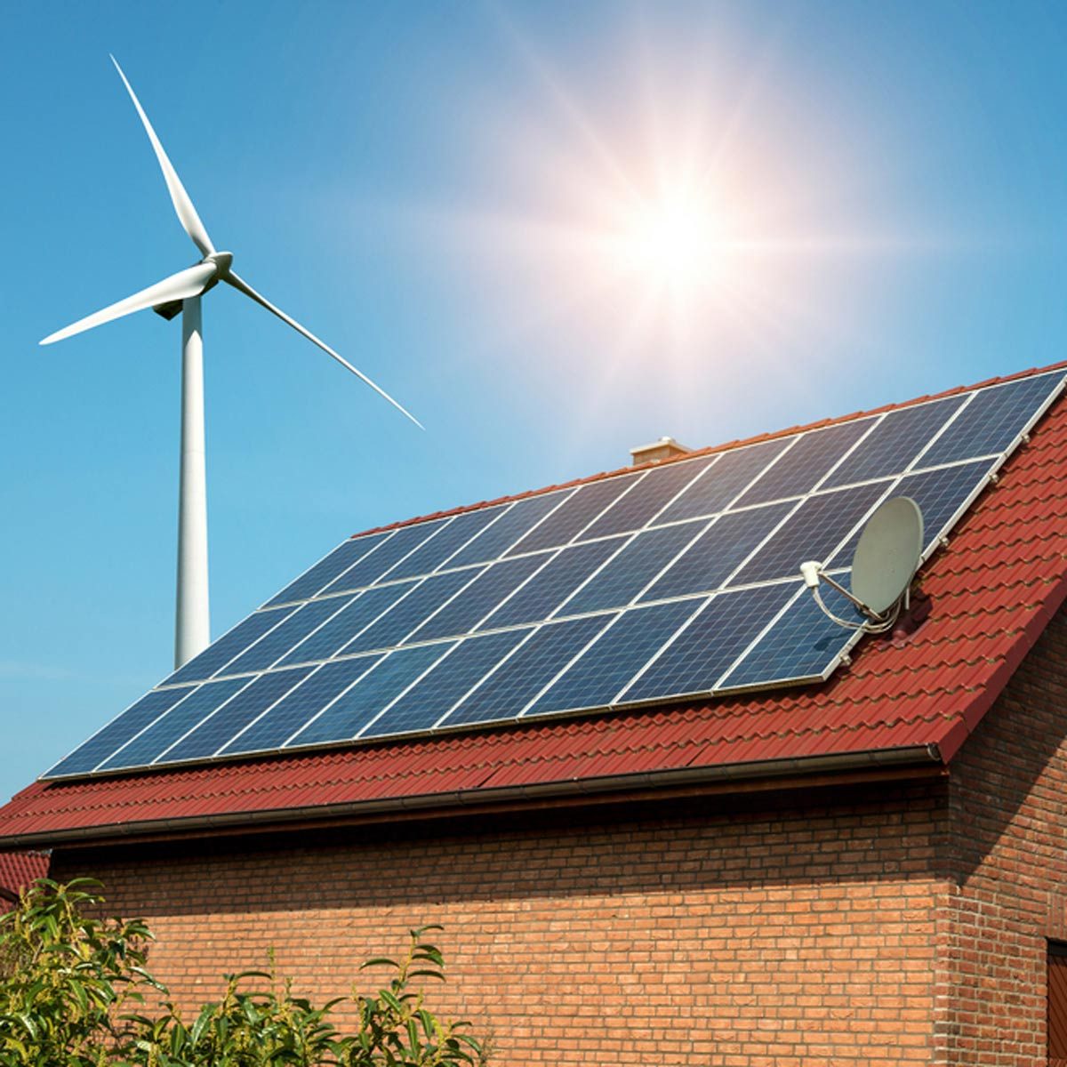 A house features solar panels on the roof, while a wind turbine stands nearby, under a bright sunlit sky.