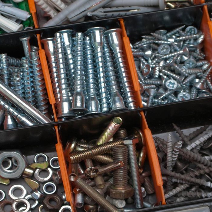 Various metallic screws, bolts, and nuts are organized in a divided storage container, illustrating a cluttered but organized workspace for hardware or DIY projects.