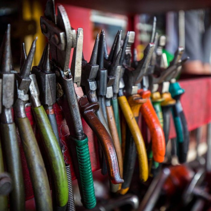 A collection of pliers hangs on a red rack, showcasing various colors and sizes, set in a workshop environment filled with other tools.
