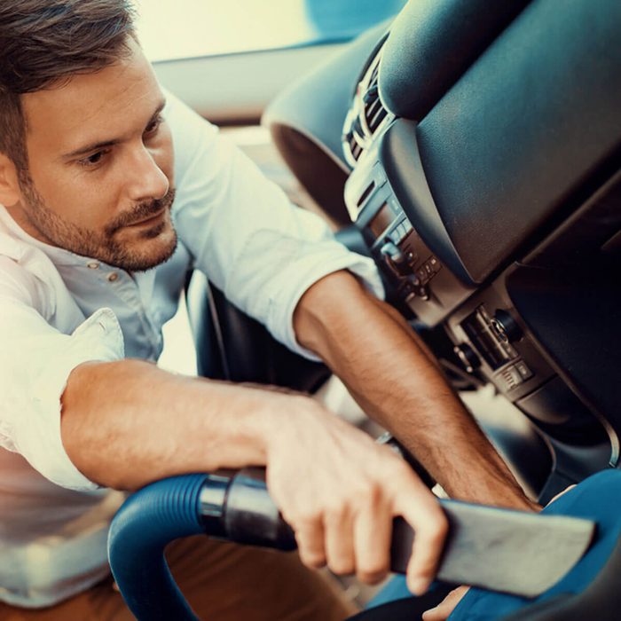 A man vacuums the interior of a car, focusing on the dashboard and seats, revealing a clean and organized vehicle environment.