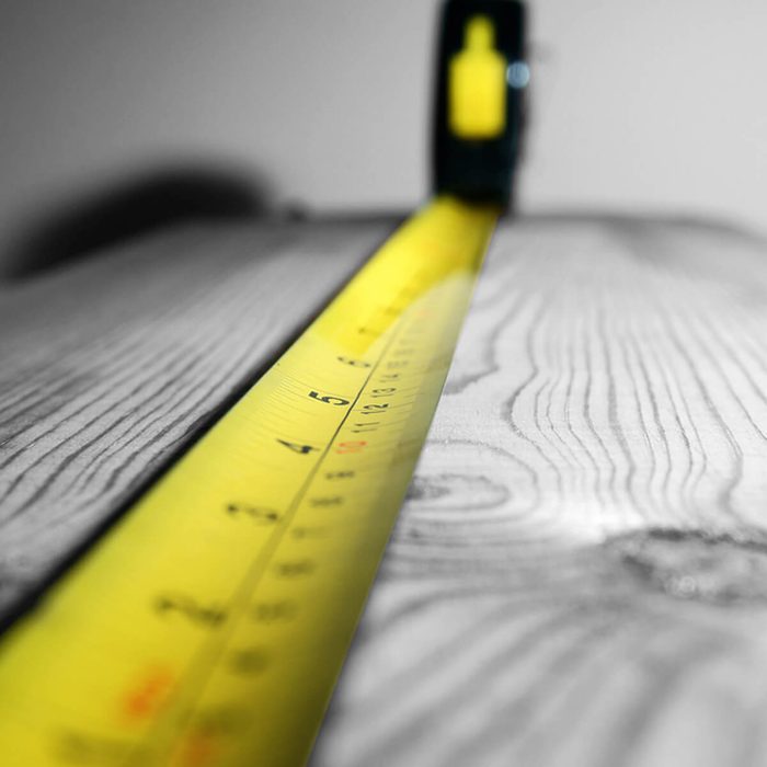 A yellow measuring tape extends across a wooden surface, indicating measurements against a blurred background, emphasizing precision in a construction or DIY context.