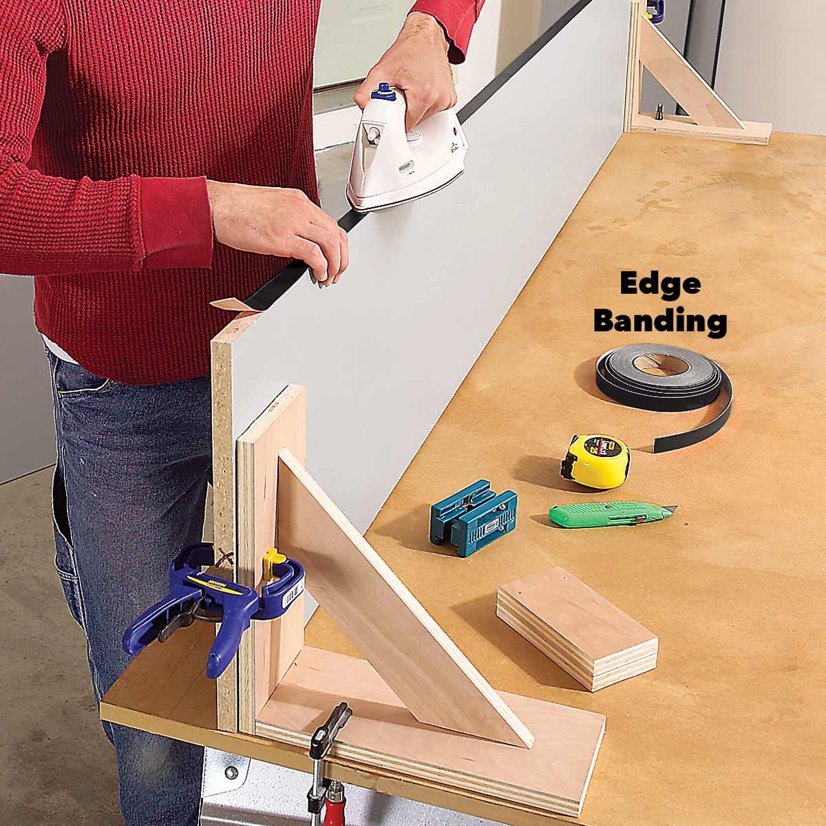 A person uses an iron to apply edge banding to a board on a workbench, surrounded by tools like a tape measure, clamps, and a utility knife.