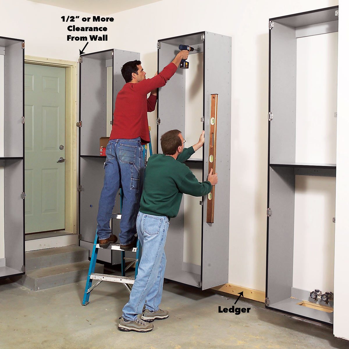 Two men work together to install shelving units, using a drill and a level in a residential setting with a door visible in the background.