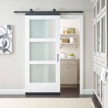 A sliding glass door partially opens to reveal a modern kitchen with organized shelves, light cabinets, and fruit bowls, against a neutral wall.