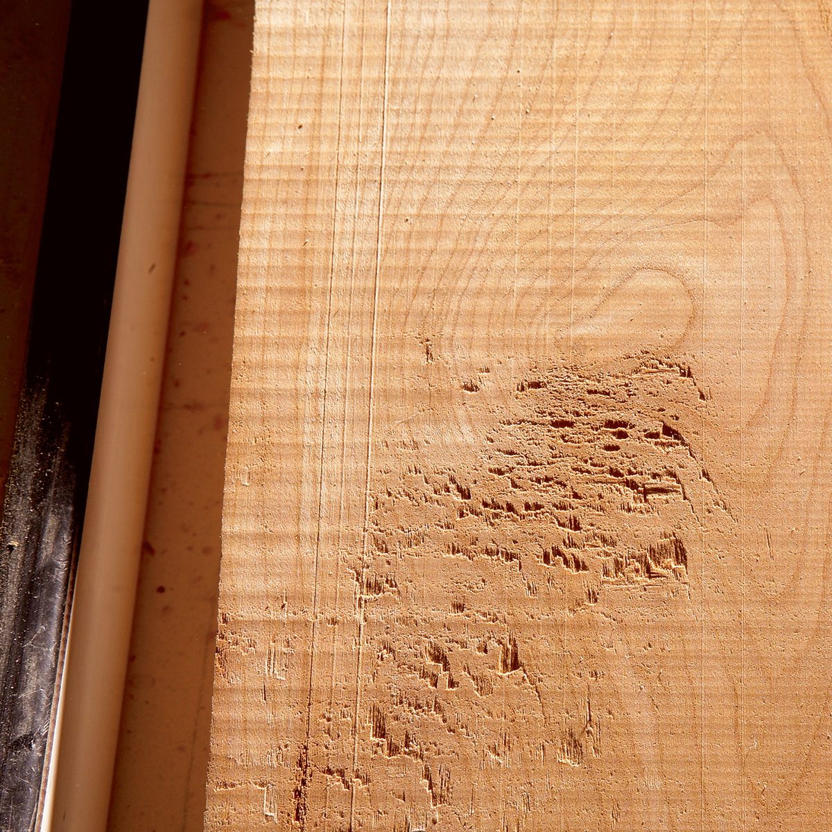 A wooden surface displays texture and scratches, revealing marks likely from cutting tools. A black and white edge suggest a working environment, possibly a workshop.