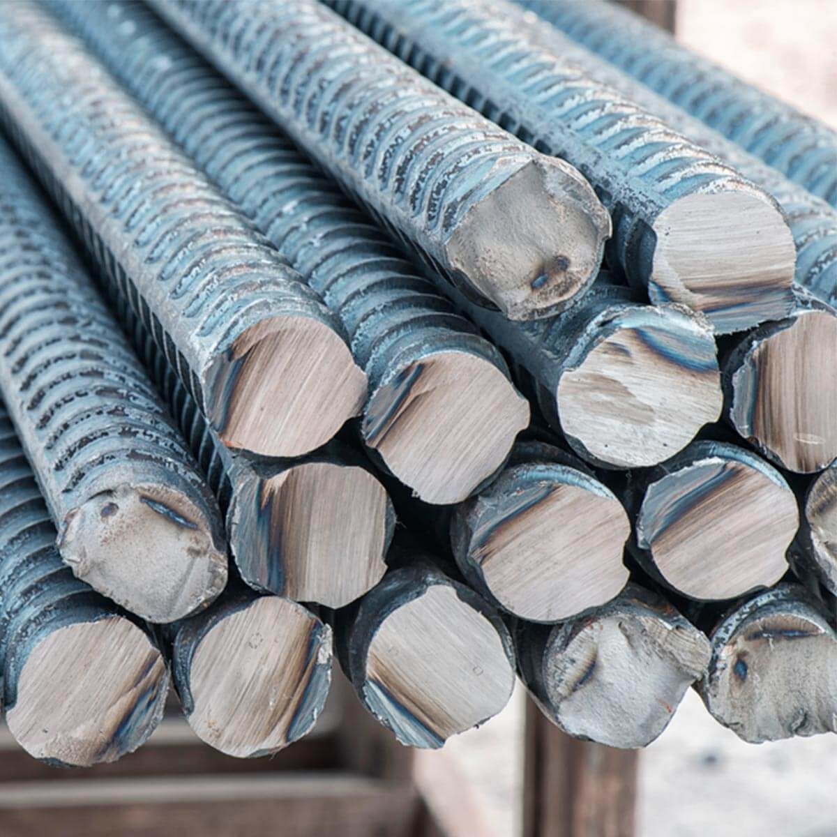 Steel reinforcing bars lie stacked in close proximity, showcasing their textured surfaces and cut ends in a construction environment.