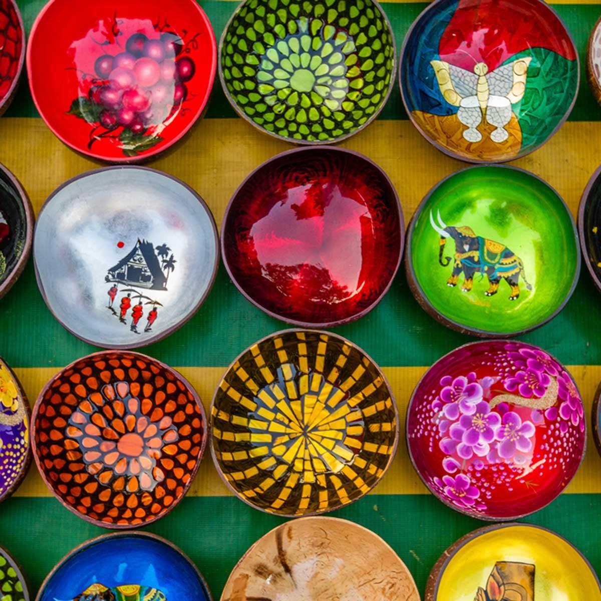 Colorful, hand-painted bowls arranged in a grid, displaying various intricate designs against a striped background, showcasing vibrant artistry and craftsmanship.
