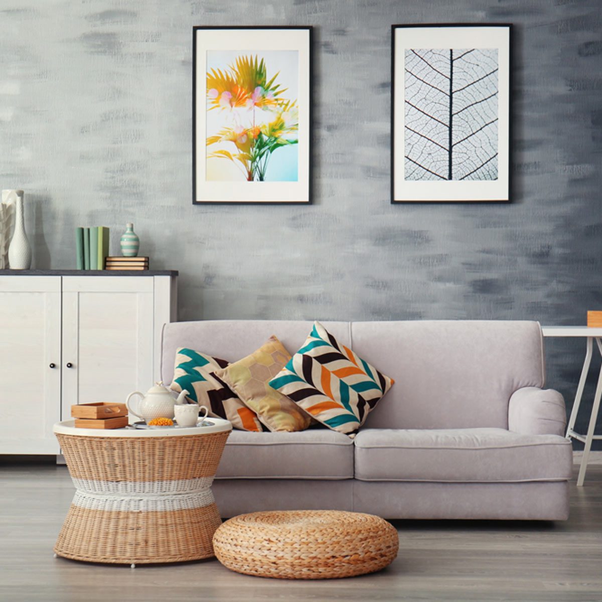 A comfortable sofa with decorative pillows sits beside a woven coffee table, adorned with tea and snacks, against a stylishly painted wall with framed art.