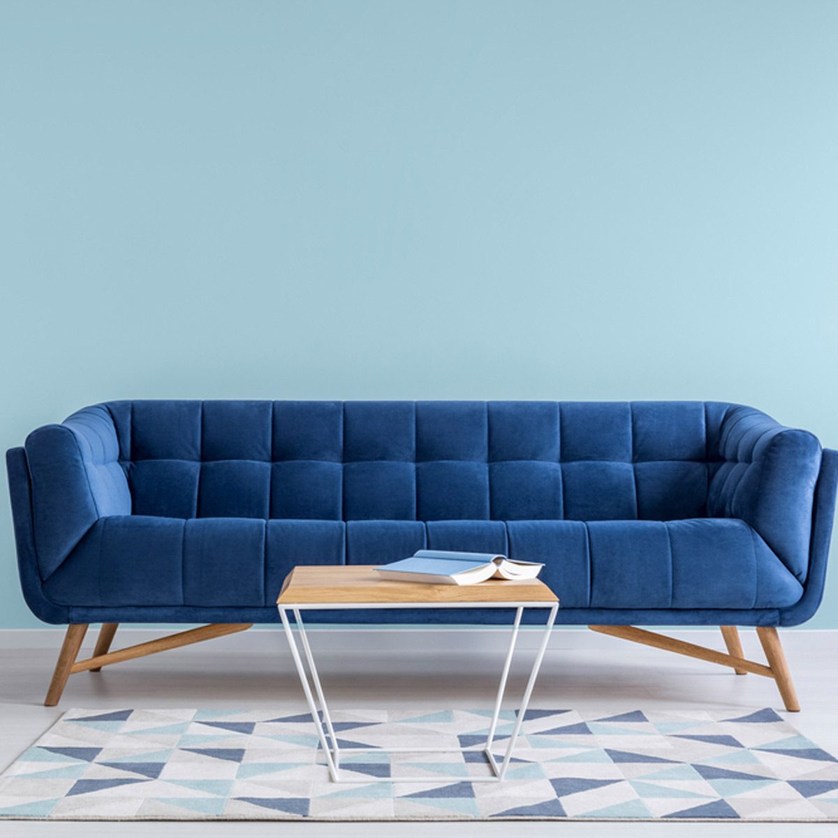 A blue couch rests against a light blue wall, with a wooden coffee table in front. A book lies open on the table, next to a closed book.
