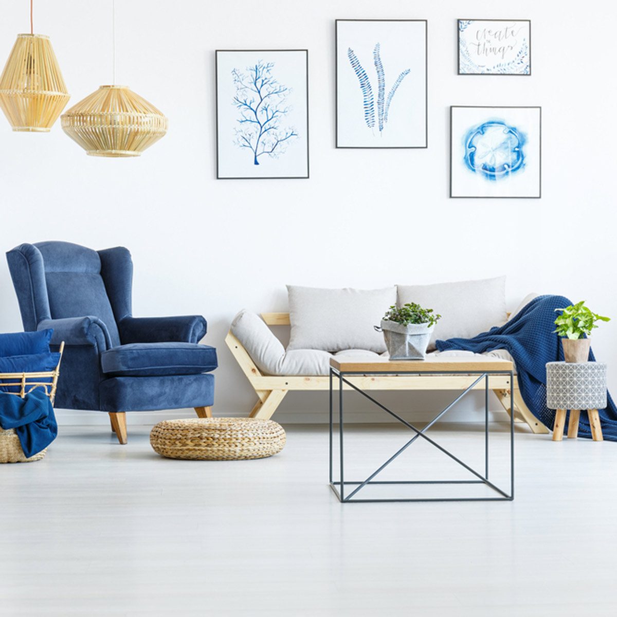 A cozy living room features a blue chair, light wooden sofa, and a coffee table. Wall art adds character against a bright, minimalist background.