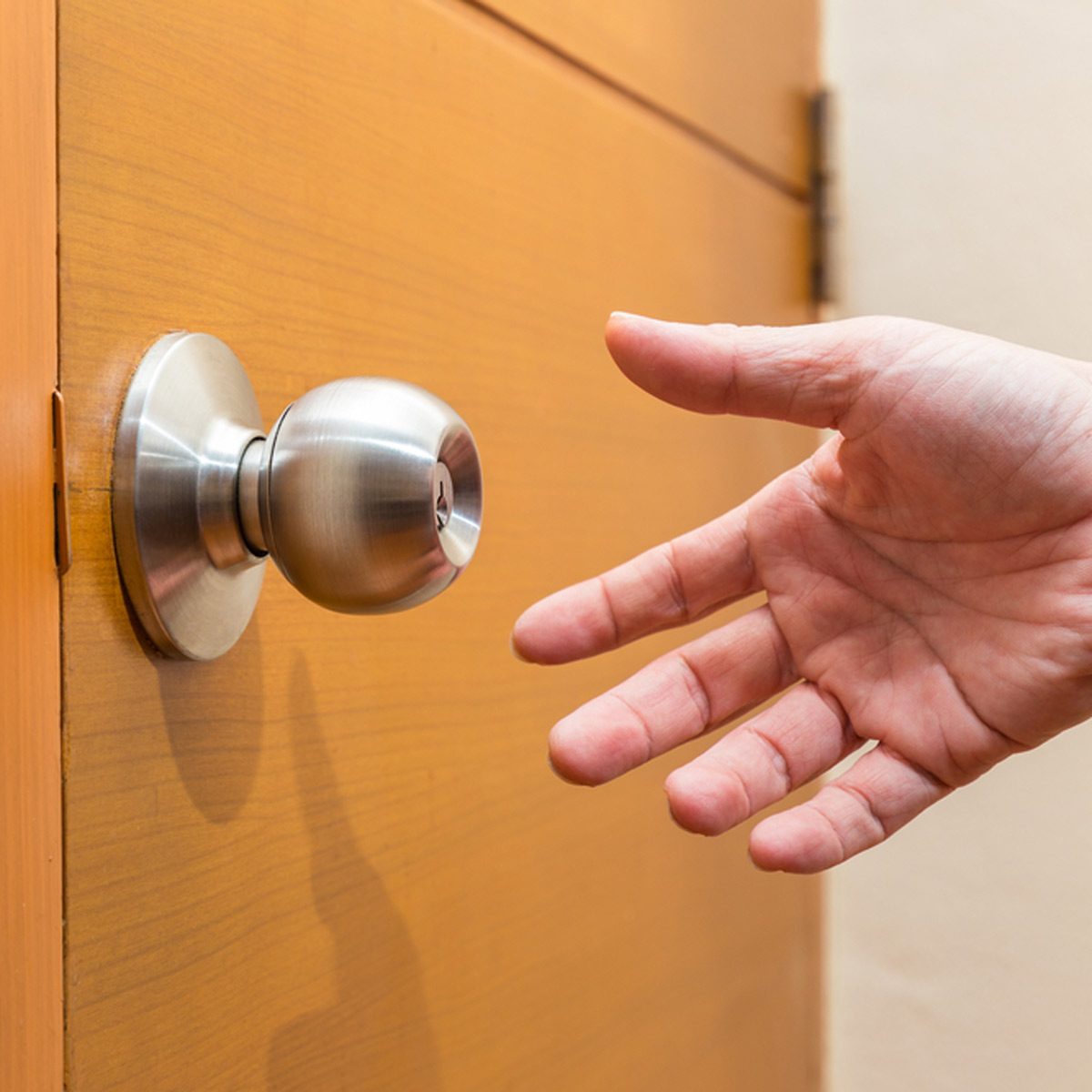 A hand reaches toward a metallic doorknob on a wooden door, preparing to grasp it for entry. The surrounding area appears minimal and uncluttered.