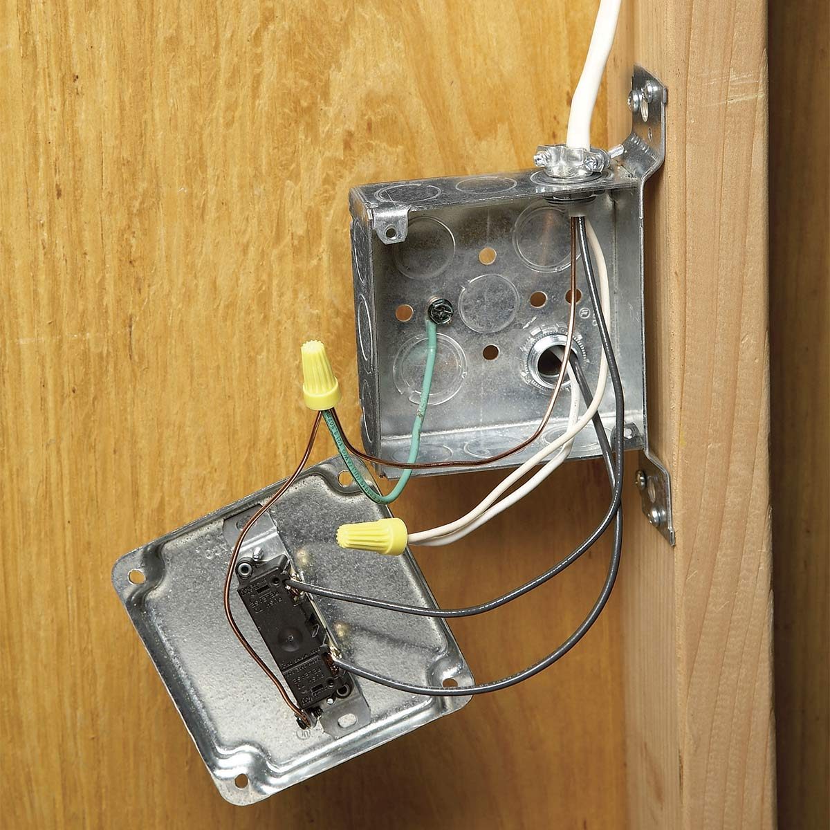 A metal electrical box with exposed wires is mounted on a wooden surface. Some wires are combined with connectors while one side is detached.