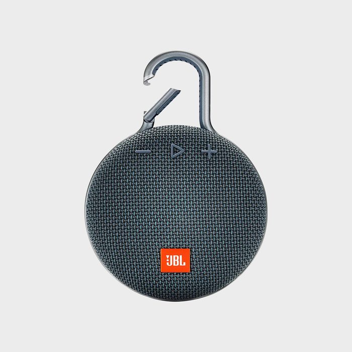 A round, portable Bluetooth speaker hangs from a hook, featuring control buttons and a textured surface, ideal for outdoor use.