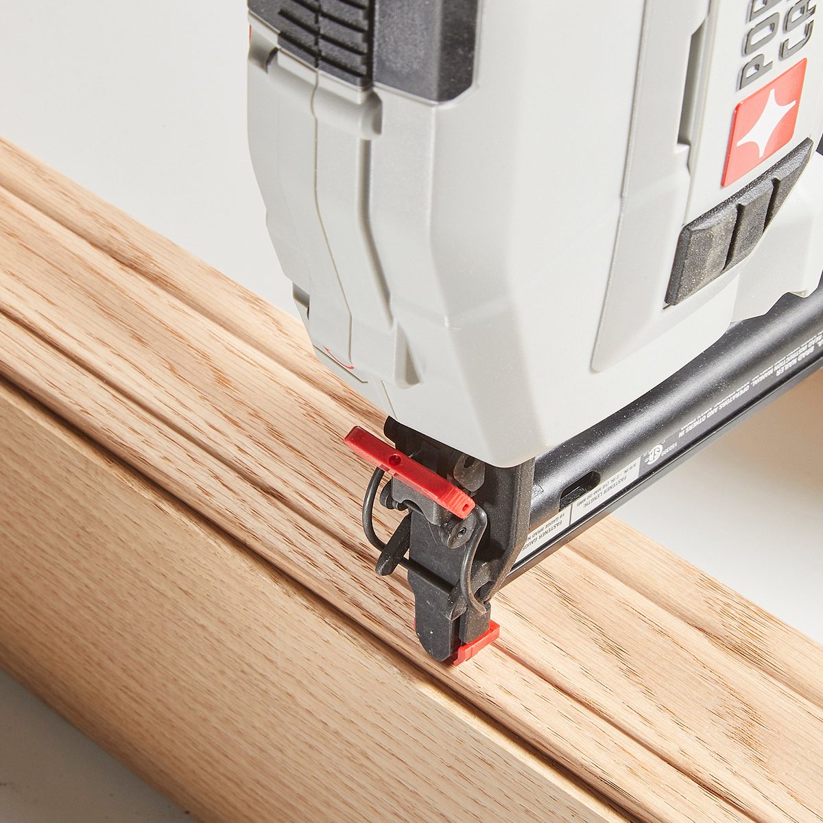 A nail gun is positioned above a wooden surface, ready to fasten materials together, indicating an ongoing woodworking project in a workshop environment.