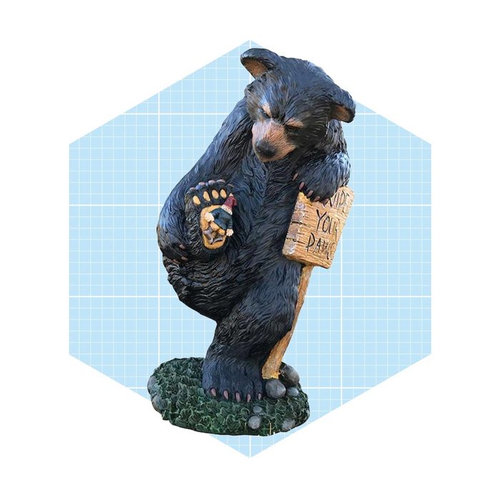 A black bear figurine stands on a grassy base, holding a wooden sign that reads 