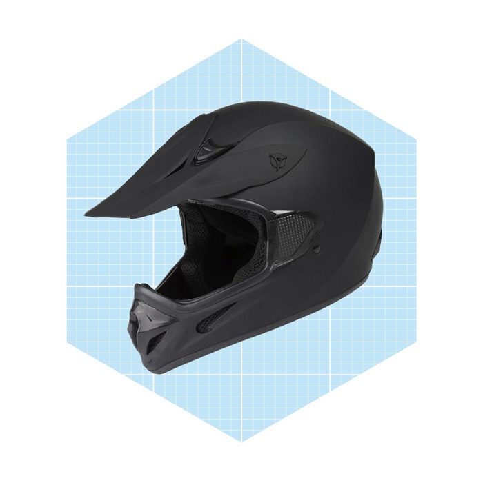 A black motorcycle helmet rests on a light blue grid background, designed for off-road use with a prominent visor and ventilation openings.