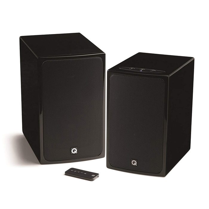 Two black speakers sit side by side, emitting sound, accompanied by a small remote control for adjusting settings. The surface is smooth and reflective.