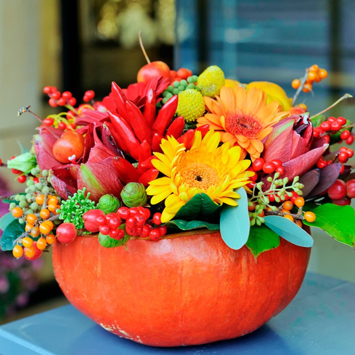 A pumpkin serves as a vibrant vase filled with assorted colorful flowers and berries, set against a softly blurred background.