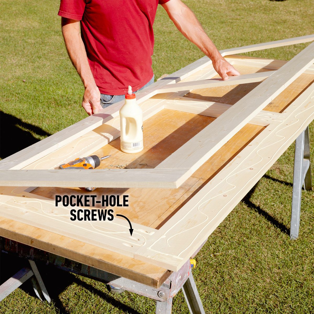 A person applies glue to wooden pieces on a workbench, preparing to assemble them using pocket-hole screws, set in a grassy outdoor environment.