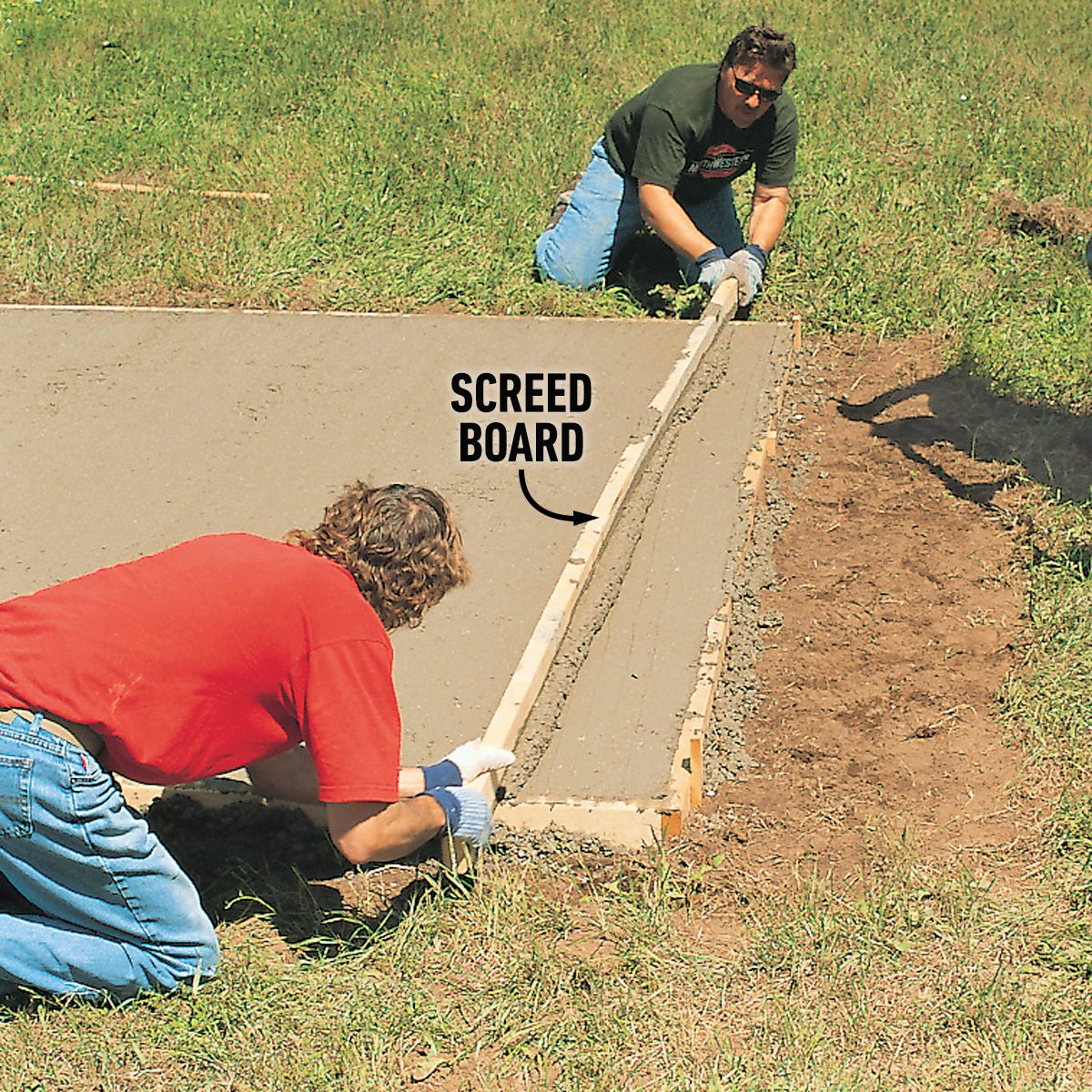 Two people are leveling wet concrete using a screed board in a grassy outdoor area. Soil and tools are visible nearby.