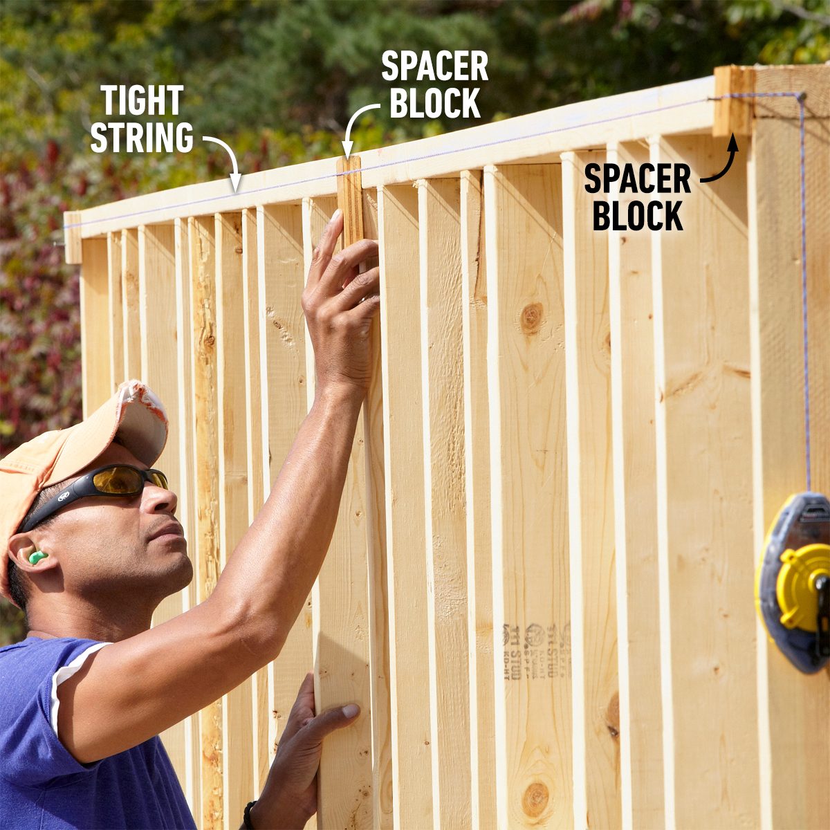 A person adjusts a spacer block against wooden framing, ensuring alignment with a tight string, in an outdoor construction setting.