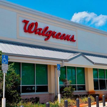 Walgreens sign displayed on a pharmacy building; green-tinted windows and accessible parking signs are visible, set against a clear blue sky.