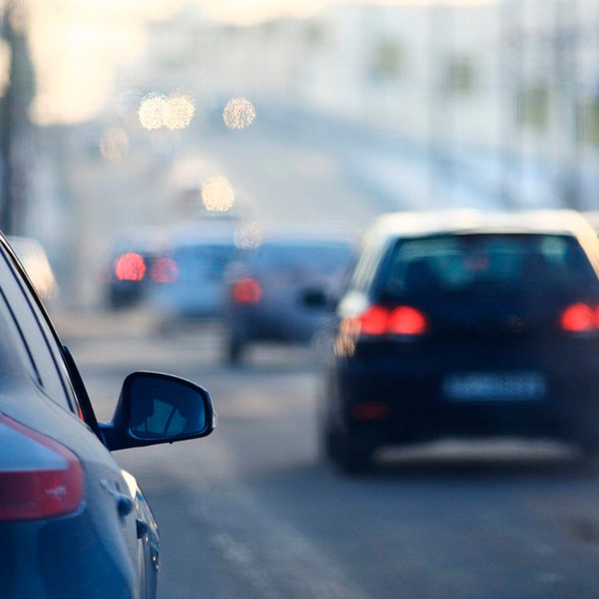 A blue car is parked on a busy street, while other vehicles are driving in the background, blurred by depth of field.