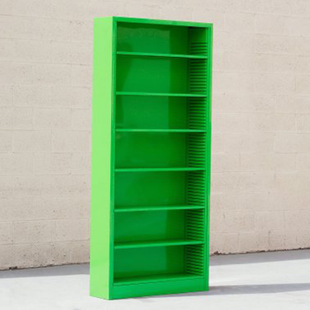 A tall, vibrant green bookshelf stands upright against a light-colored wall, featuring multiple empty shelves and a smooth, glossy finish.