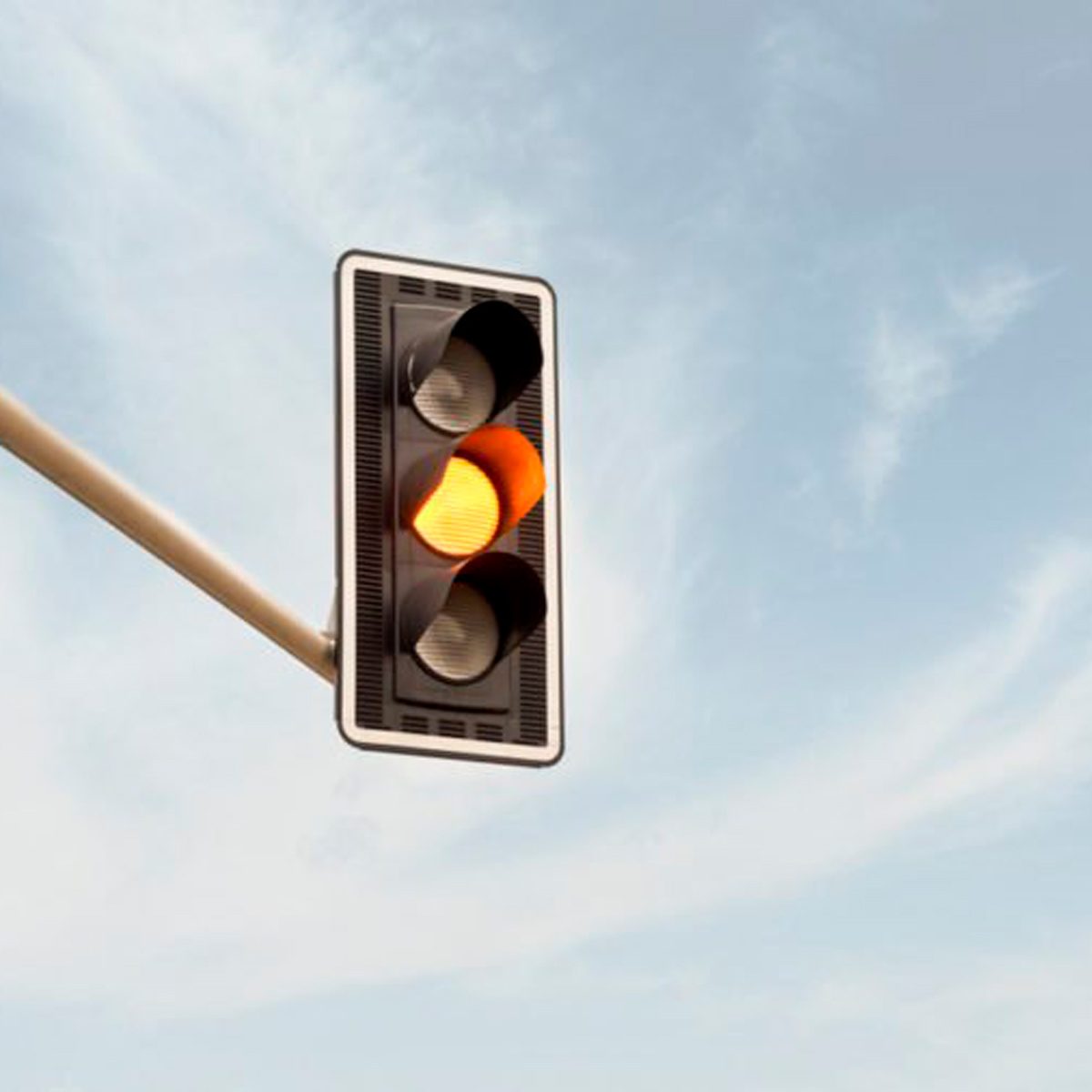 A traffic light displays a yellow signal, indicating caution as it prepares to change. The background features a clear sky with minimal clouds.