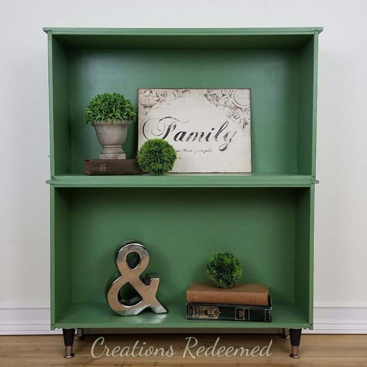 A green shelf holds decorative items, including a sign with "Family," small plants, and a metal ampersand, set against a light background.