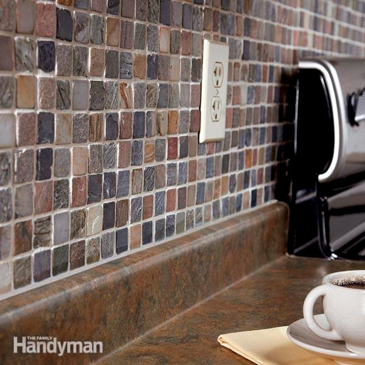 A tiled backsplash features varied small stones, with a power outlet visible. A countertop holds a coffee cup and a folded napkin beside it.