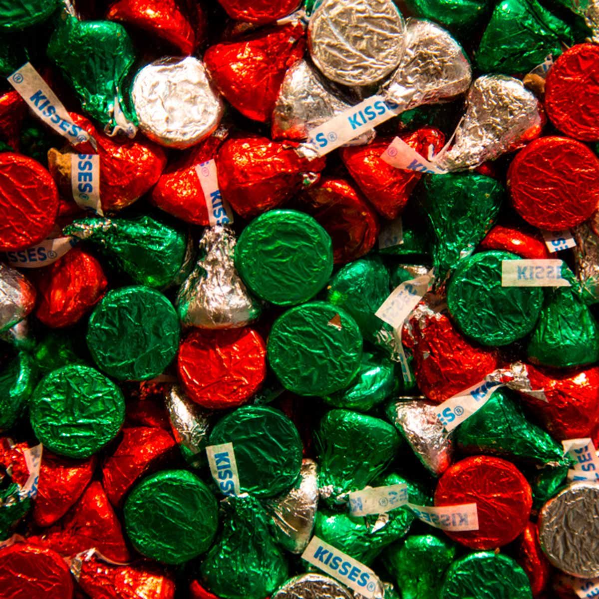 Colorful chocolate candies are piled together, wrapped in shiny red, green, and silver foil, showcasing a festive arrangement suitable for celebrations.