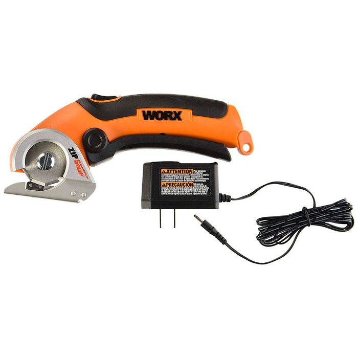 A battery-operated cutting tool with a circular blade rests beside its power adapter, designed for precision cutting in various materials.
