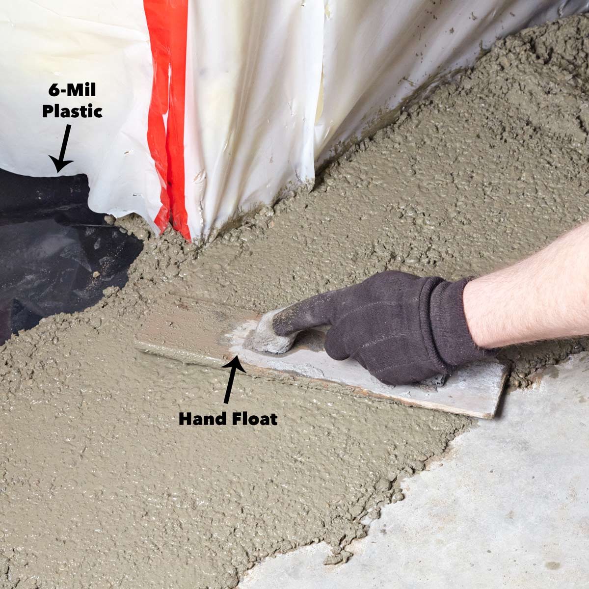 A hand float smooths fresh concrete on the ground, near a protective plastic barrier labeled "6-Mil Plastic," in a construction environment.