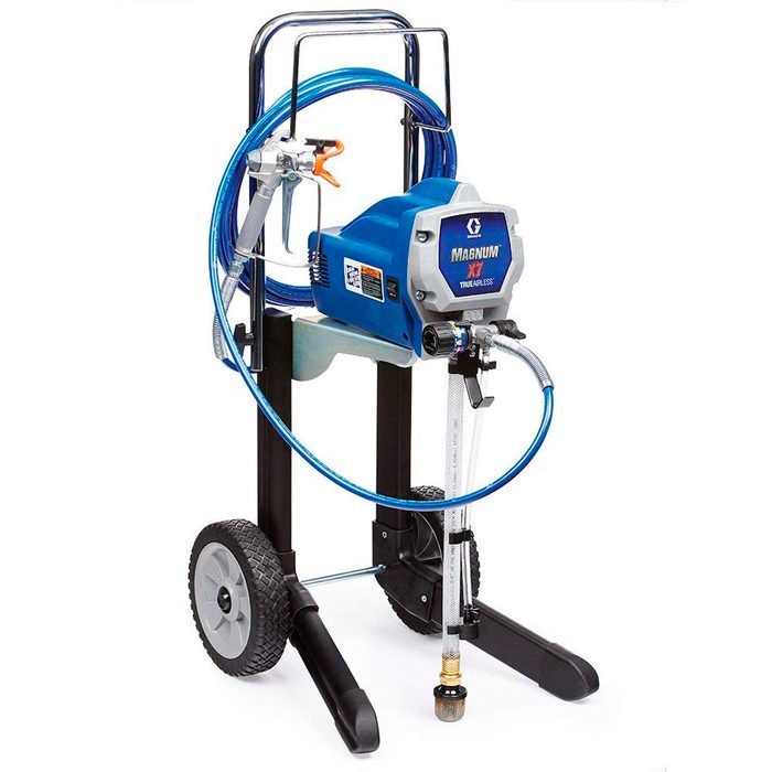 A blue airless paint sprayer rests on a wheeled stand, equipped with hoses and a spray gun, ready for use in painting projects.