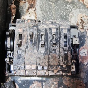 A dusty electrical circuit breaker panel displays several switches in various positions, situated on a worn, stained surface with debris around.
